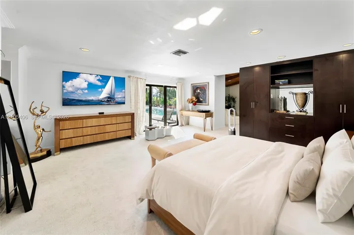 Recessed lighting, light-toned carpeting, built-in dark wood cabinetry, glass sliding doors, and white walls