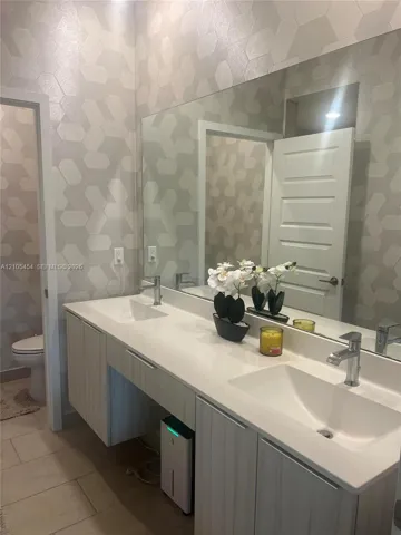 Dual rectangular basin vanity with chrome faucets, a full-width mirror, and geometric pattern wall covering
