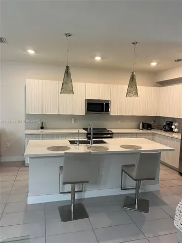 Modern kitchen featuring white cabinetry, a large kitchen island with integrated sink, recessed lighting, and two pendant light fixtures