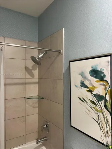Bathtub with a tiled surround, a glass corner shelf, a brushed nickel showerhead, and a matching tub spout