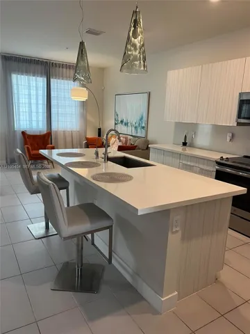 Kitchen island with integrated sink, white countertops, and modern pendant lighting