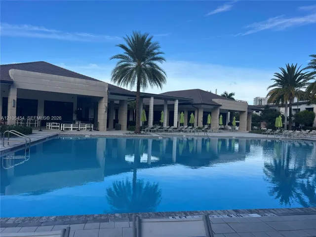 Expansive outdoor pool with integrated steps, surrounded by a paved deck and a covered patio area with recessed lighting
