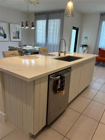 Kitchen island featuring a single-basin sink, gooseneck faucet, integrated dishwasher, and light-toned cabinetry