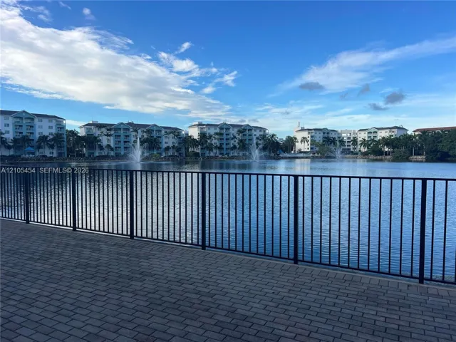 Paver patio with black metal railing overlooking a tranquil lake with water features