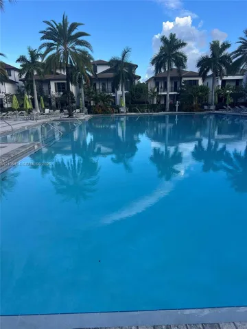 Resort-style swimming pool bordered by residences with balconies and mature palm trees