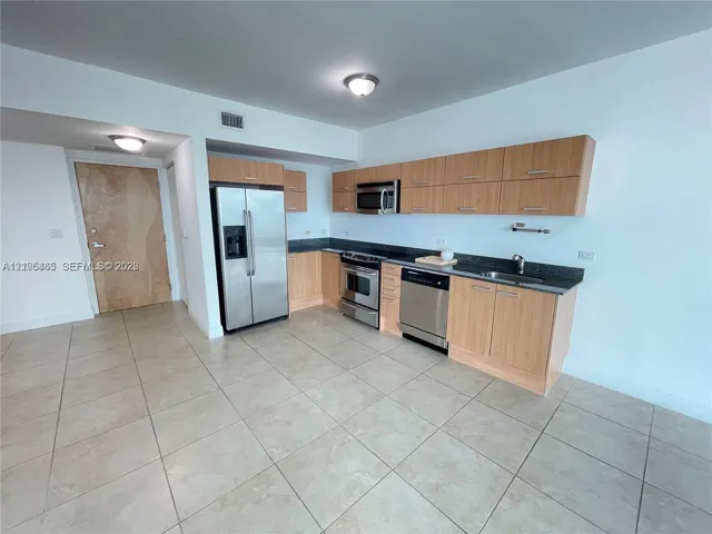 Kitchen featuring light wood-finish cabinetry, stainless steel appliances, dark countertops, and tile flooring