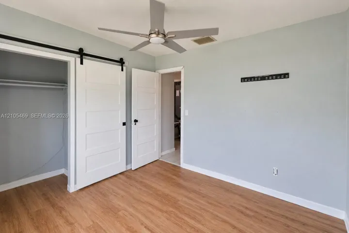 Wood-finish flooring, ceiling fan, white barn doors, and light gray wall paint