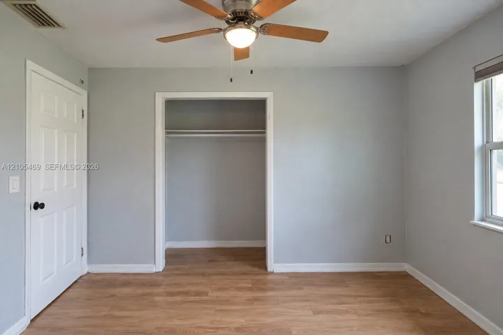 Wood-finish flooring, ceiling fan with integrated lighting, window with roller shade, and an open closet space