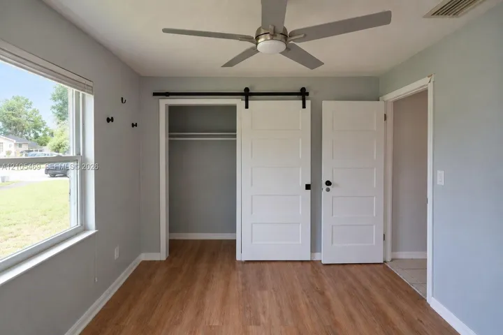 Wood-finish flooring, ceiling fan with integrated lighting, sliding barn door closet, and white panel doors