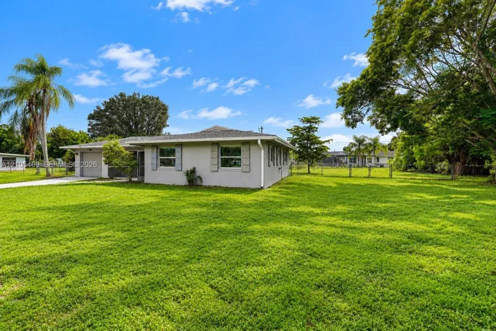 Spacious green lawn surrounding the property, featuring a single-story residence with a gray exterior, a two-car garage, and mature trees