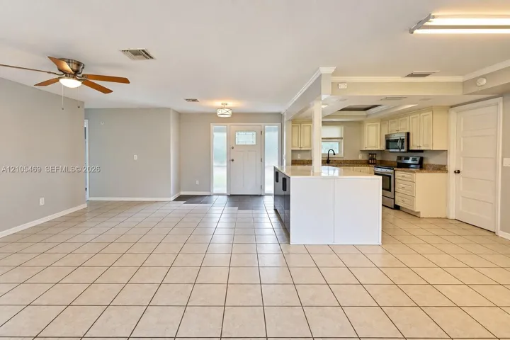 Open-concept living area with tile flooring throughout, featuring a kitchen with light-toned cabinetry, stainless steel appliances, and a central island with a breakfast bar