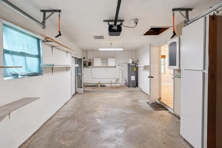Attached garage with concrete flooring, built-in shelving, overhead lighting, and a water heater