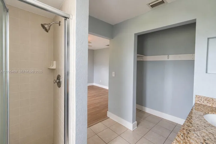 Shower enclosure with tiled walls and brushed nickel fixtures, vanity with a stone-finish countertop, and tile flooring