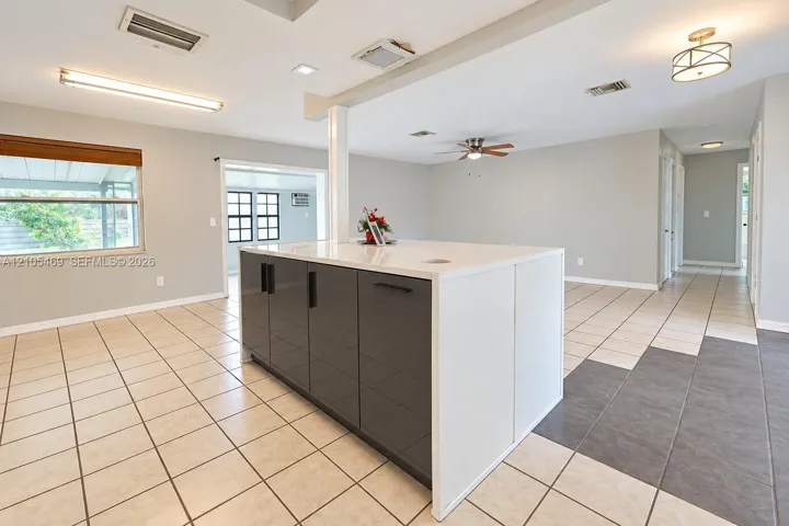 Island with a light-toned countertop, tile flooring, window with a wood-finish valance, recessed lighting, and a ceiling fan