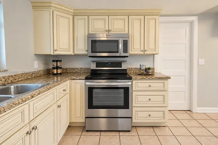Stainless steel appliances, double basin stainless steel sink, light-toned cabinetry, granite countertops, and tiled flooring