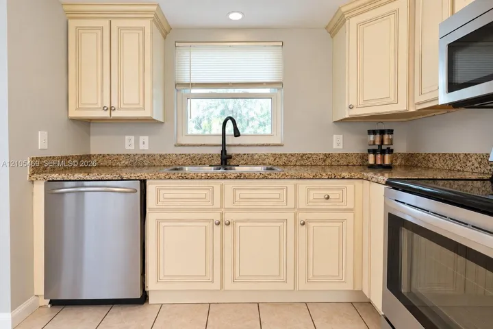 Kitchen featuring light wood-finish cabinetry, speckled countertops, stainless steel appliances, and a black faucet