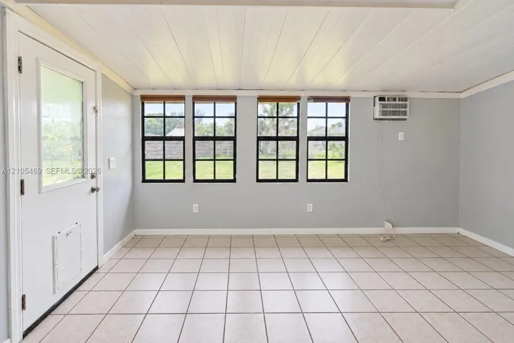 Tile flooring, four windows with dark frames, light gray walls, white paneled ceiling, and a white exterior door