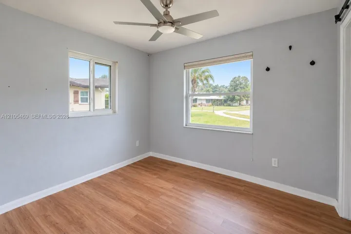 Wood-finish flooring, two windows with exterior scenery, a ceiling fan with integrated lighting, and a white interior door