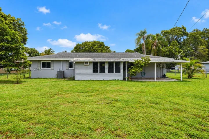 Expansive grassy backyard featuring a covered patio, mature trees, and a utility shed