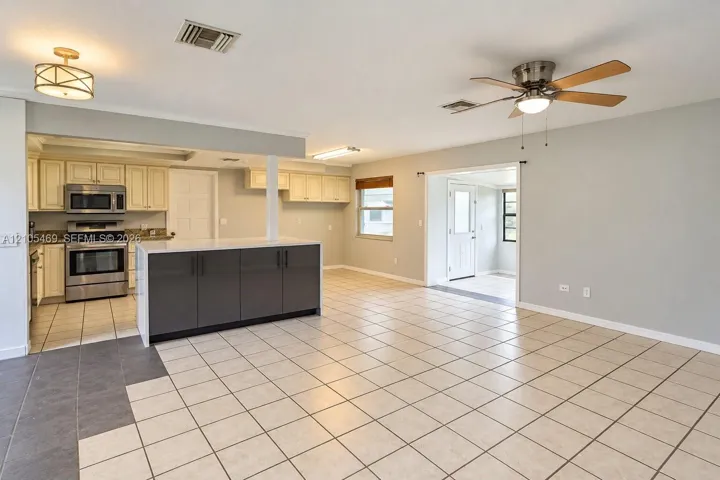 Open-concept living space featuring a central island with dark cabinetry, tile flooring, stainless steel appliances, and a ceiling fan