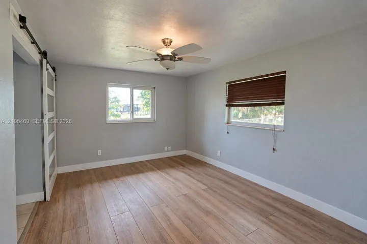 Wood-finish flooring, ceiling fan, white barn door with frosted panels, and two windows with blinds