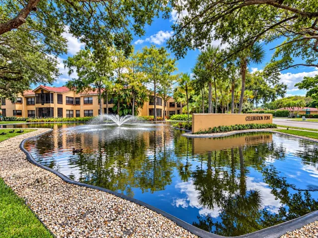 Community entrance featuring a central fountain, pond, landscaped grounds, mature trees, and rock-edged hardscaping