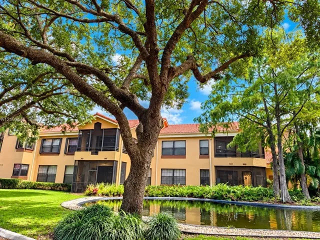 Stucco exterior with a tiled roof, screened balconies, and mature landscaping surrounding a central pond