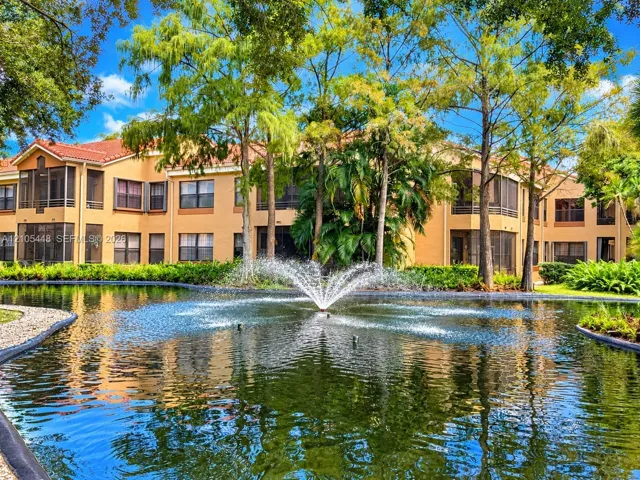 Pond featuring a central fountain, screened-in balconies, terracotta-toned tile roof, and mature perimeter landscaping