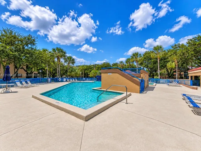 Swimming pool with a raised concrete deck, surrounding metal fencing, and mature palm trees