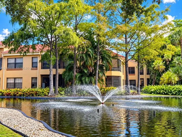 Multi-story building with a tile roof and stucco exterior, featuring an ornamental pond with a fountain, stone-lined path, and mature landscaping