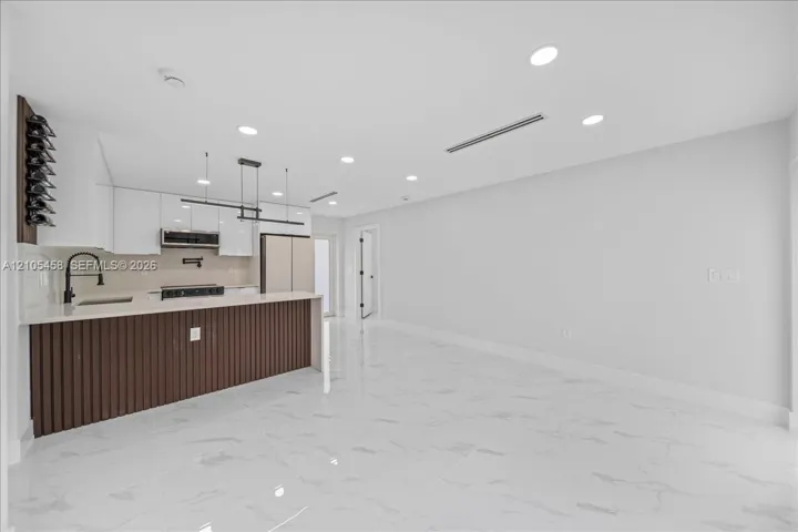 Kitchen island with vertical slat wood-finish paneling, white shaker-style cabinetry, a built-in wine rack, and a linear pendant light fixture