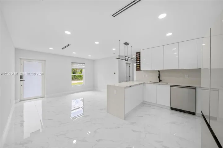 Open-concept layout featuring white high-gloss cabinetry, stainless steel dishwasher, integrated wine storage, white quartz countertops, and recessed lighting