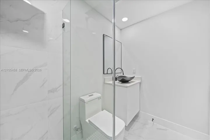 Glass-enclosed shower with large format tile surround, recessed lighting, modern vanity with vessel sink, and wall-mounted mirror