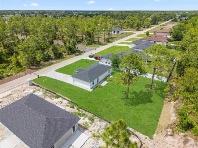 Manicured lawn, paved driveway, mature trees, newly installed roof, and surrounding natural foliage