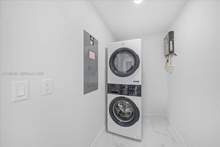 Stacked laundry appliances with a front-loading washer and dryer, recessed lighting, and large format floor tiling