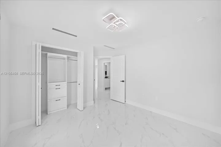 White tile flooring with subtle veining, modern ceiling light fixture, bi-fold closet doors, built-in closet organization with drawers, and a solid interior door