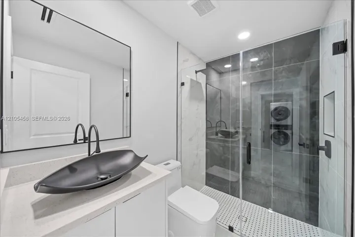 Modern bathroom featuring a glass-enclosed shower, vessel sink with matte black fixtures, white vanity cabinetry, and a light-toned countertop