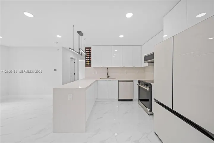 Sleek kitchen featuring white high-gloss cabinetry, stainless steel appliances, an expansive island, and recessed lighting