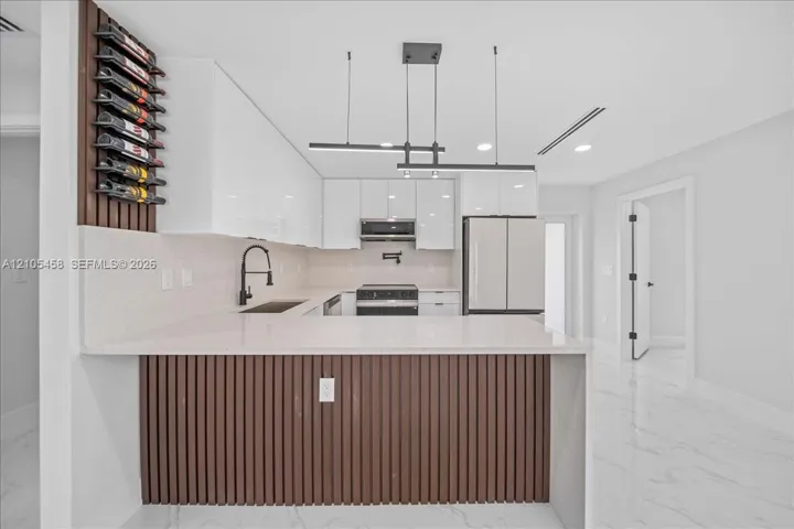Modern kitchen featuring white cabinetry, light-colored countertops, stainless steel appliances, and wood-finish paneling on the kitchen island