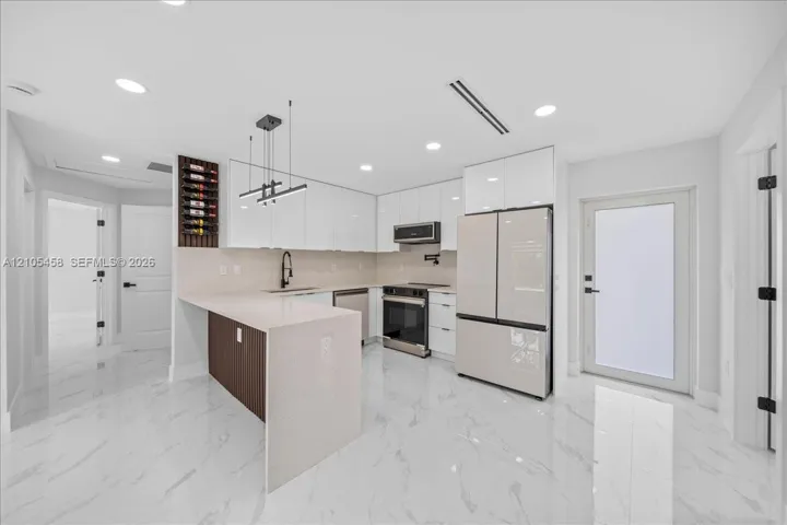 Contemporary kitchen featuring white flat-panel cabinetry, a built-in wine rack, light-toned countertops, and stainless steel appliances