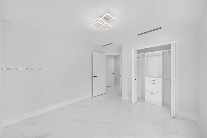 White tile flooring, contemporary ceiling light fixture, white interior doors, built-in closet organization system, recessed lighting