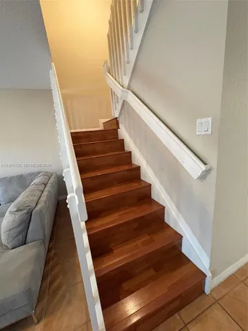 Wood-finish staircase with white risers and railings, complemented by light-toned wall paint and tile flooring
