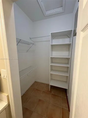 Walk-in closet with terra cotta tile flooring, white wire shelving, white storage shelving, and white walls