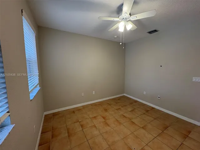 Warm-toned tile flooring, neutral wall tones, window with horizontal blinds, and a ceiling fan with integrated lighting