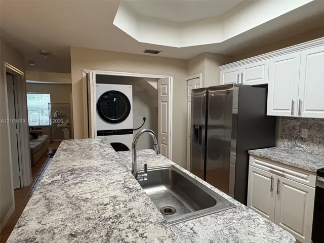 Kitchen featuring a stainless steel sink with a high-arc faucet, light-toned countertops, white cabinetry with silver-toned hardware, and a stainless steel refrigerator