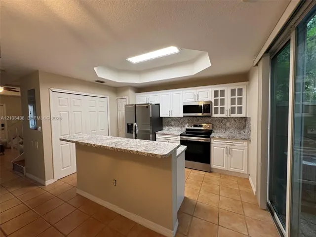Kitchen featuring stainless steel appliances, white cabinetry, granite countertops, and tile flooring