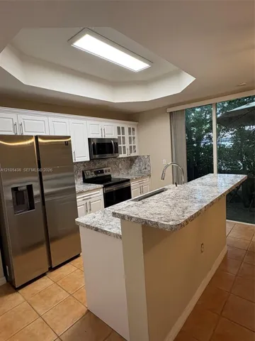 Kitchen featuring white cabinetry, light-toned countertops, tile flooring, and a stainless steel refrigerator
