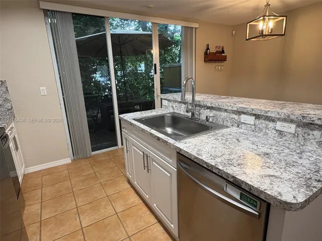 Stainless steel kitchen sink with a high-arch faucet, white lower cabinetry, and light-toned mottled countertops
