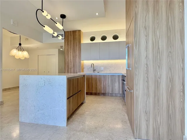 Kitchen featuring wood-finish cabinetry, a large center island with a light-toned countertop, integrated refrigeration, and unique overhead lighting fixtures