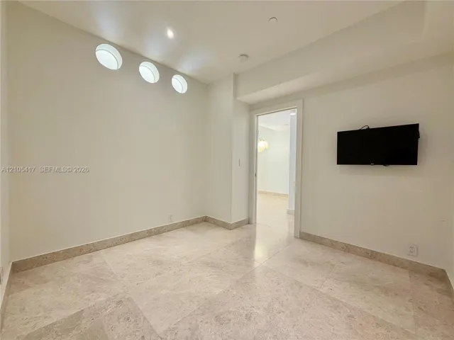 Recessed lighting, three circular wall cutouts, light-toned stone tile flooring, and a cased doorway
